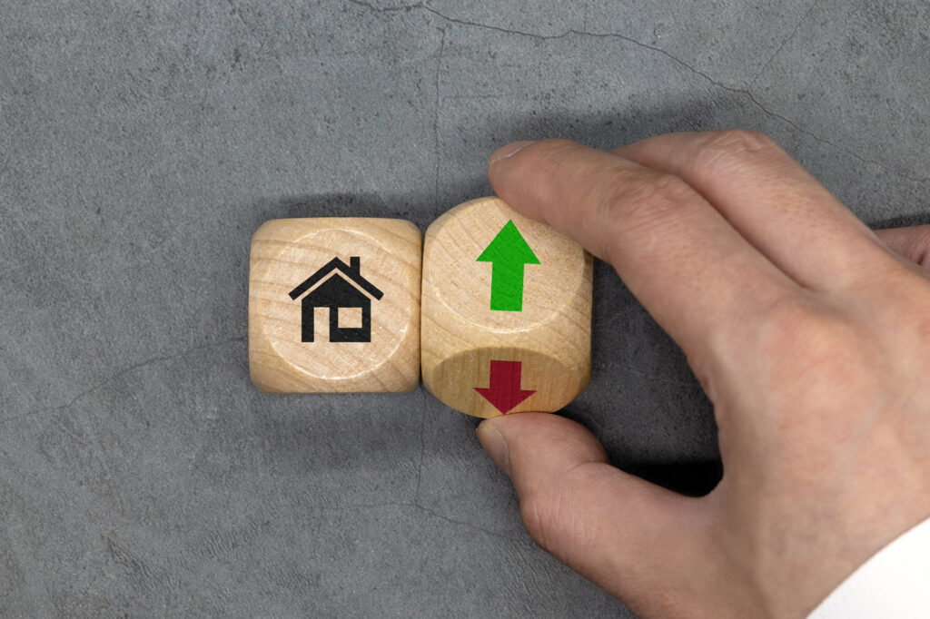 Hand turning wooden blocks showing a house icon and arrows for rising or falling property values